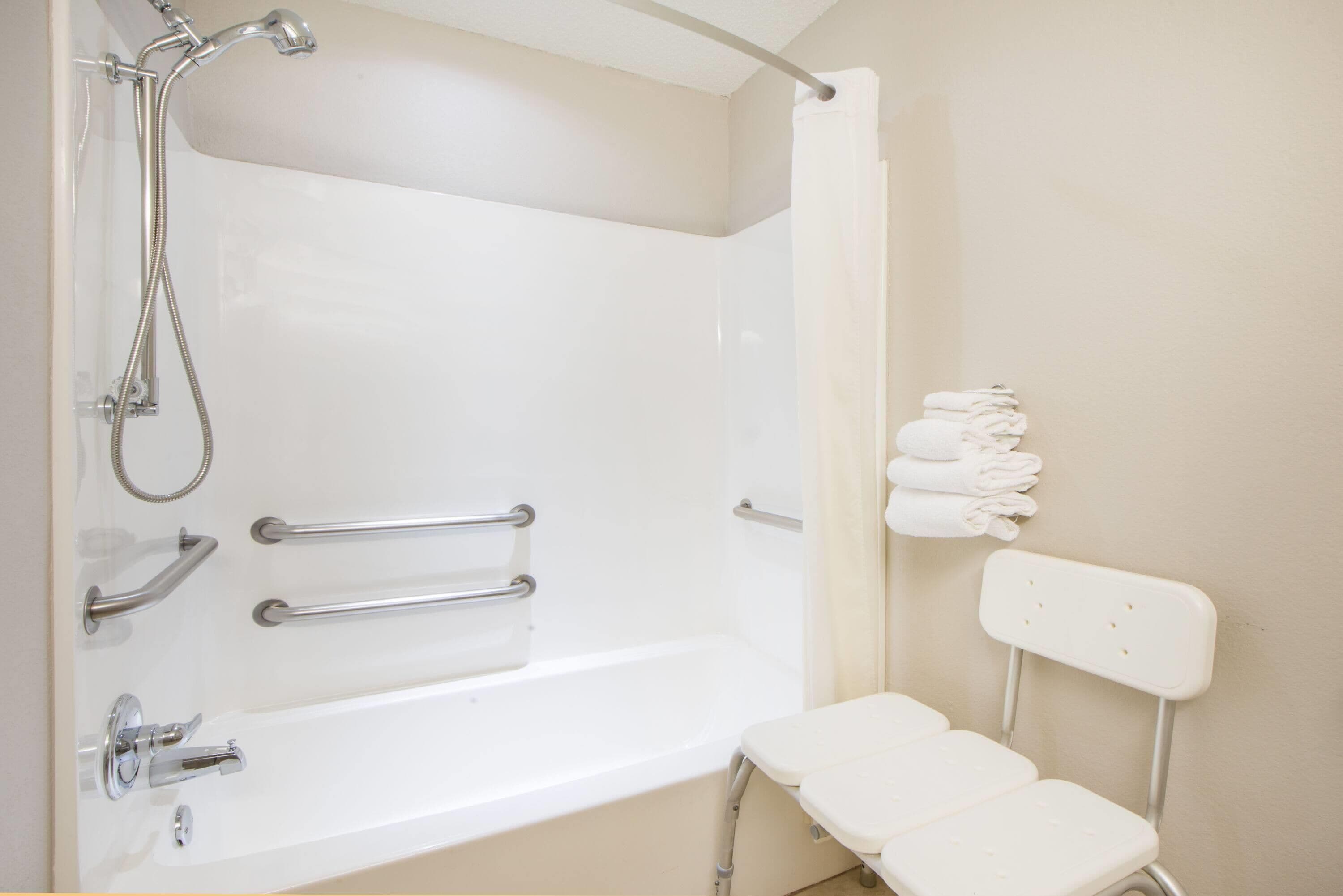Un baño con bañera, ducha, barras de apoyo y un perchero para toallas.
