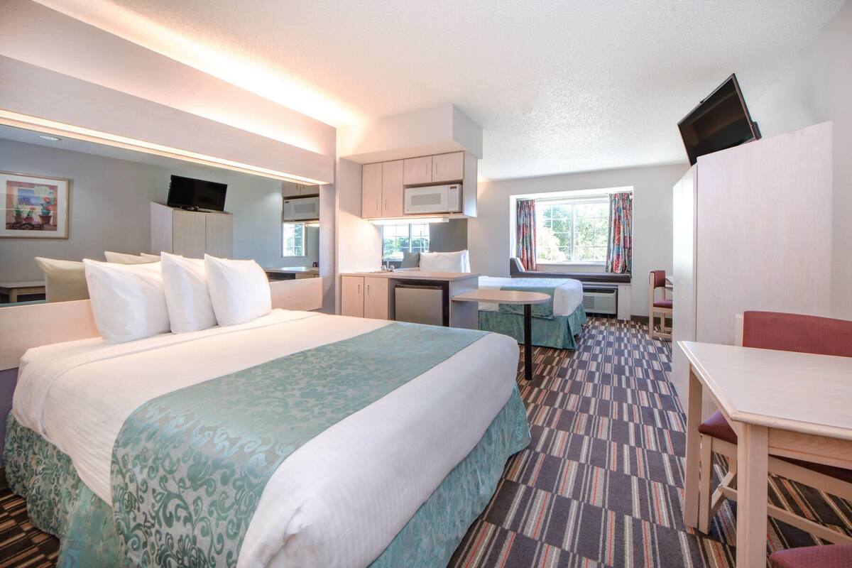 A hotel room with a bed, a desk, a chair, a television, and a window.