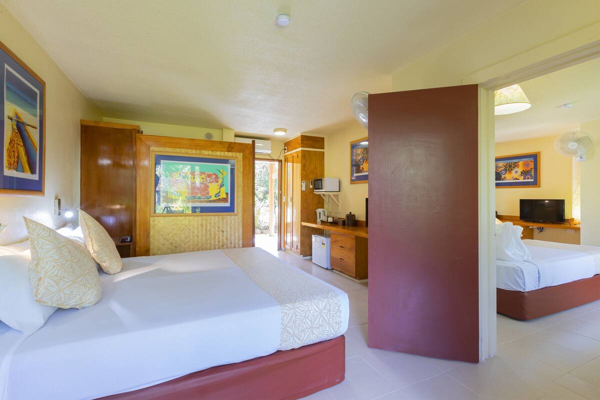 A hotel room with two beds, a desk, a television, and artwork on the walls.