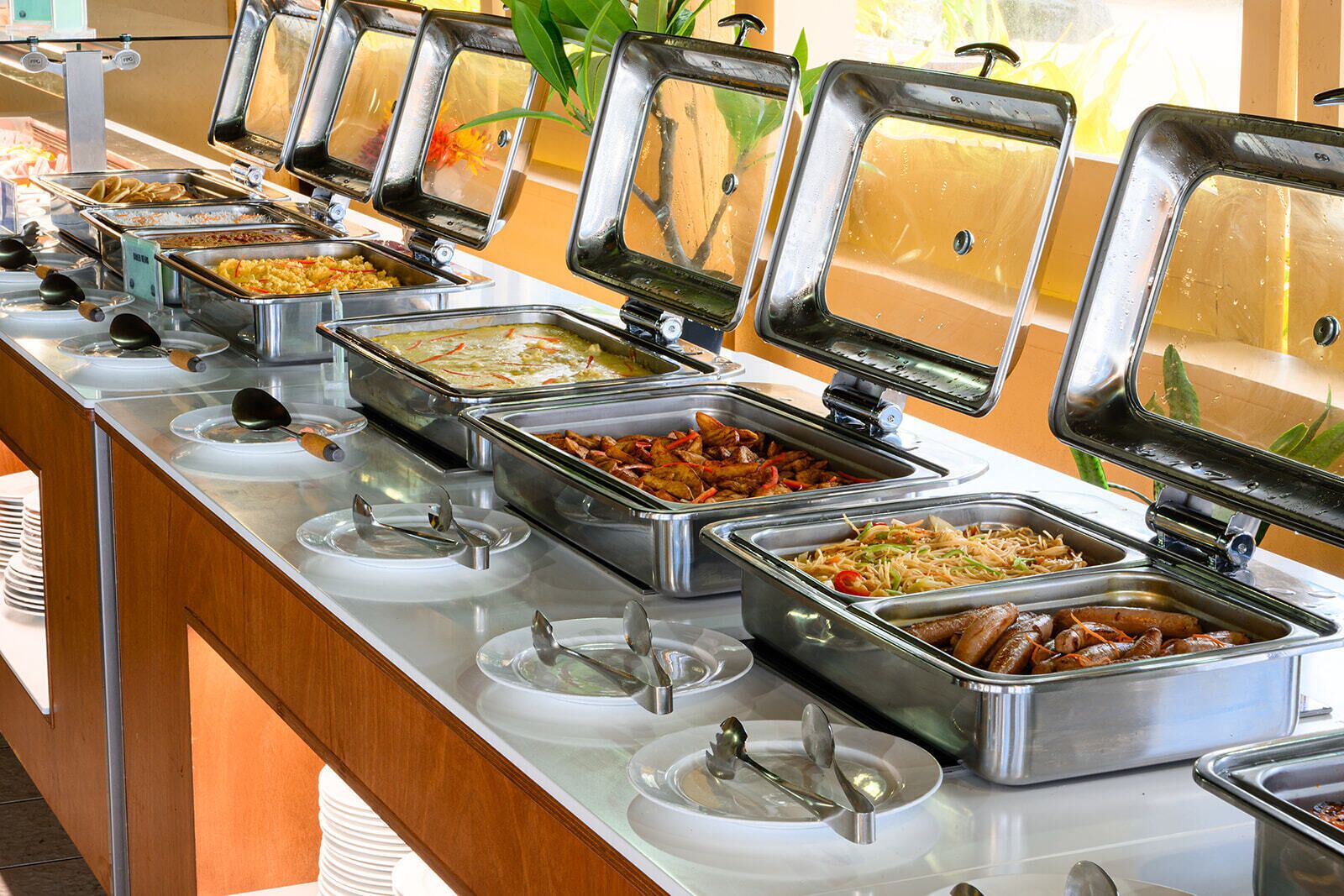 Un bufé con varias estaciones de comida, cada una con una tapa de cristal y una cuchara.