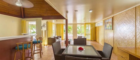 Una habitación amplia con techo alto, un comedor con muebles de mimbre y una zona de bar con taburetes.