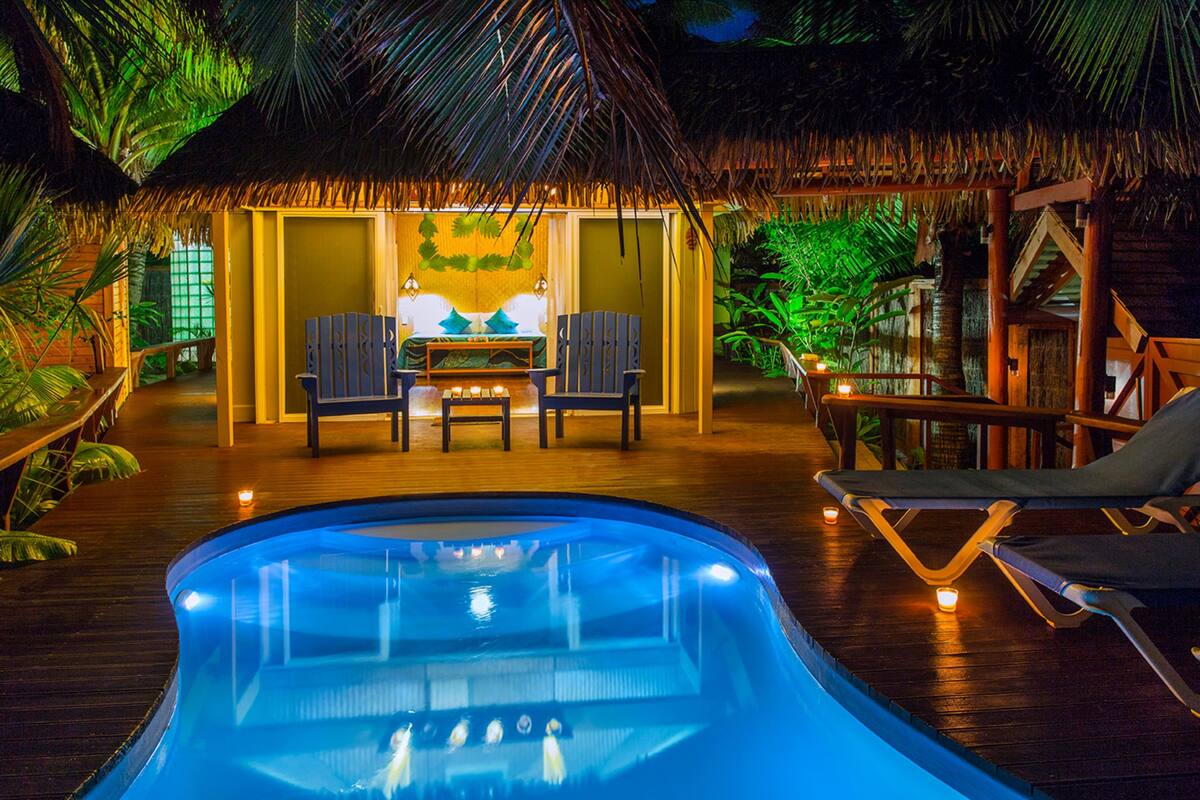 A pool area with a thatched-roof structure, lounge chairs, and a table with two chairs.