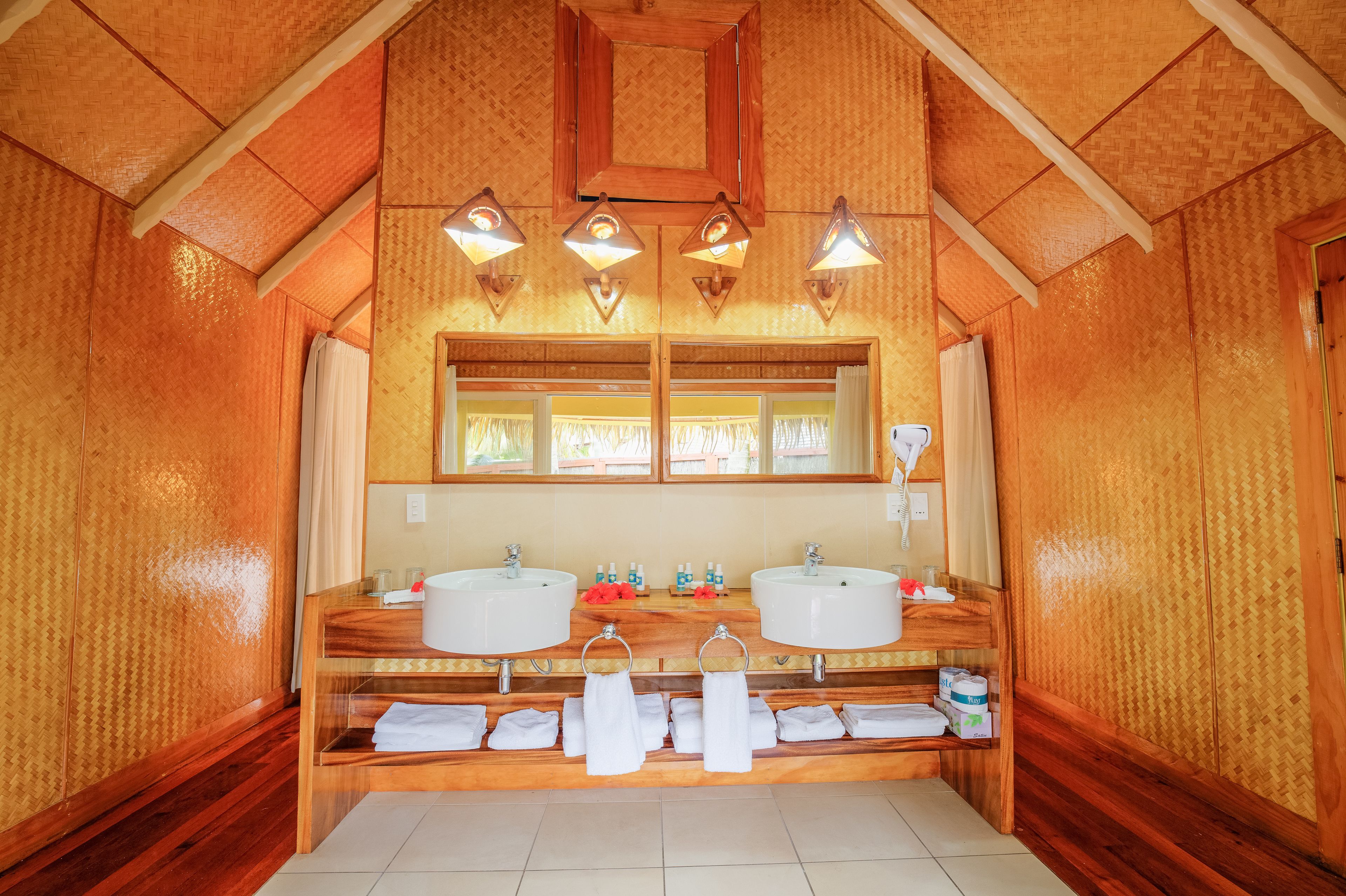 Un baño de madera con dos lavamanos, un espejo y tres luces empotradas.