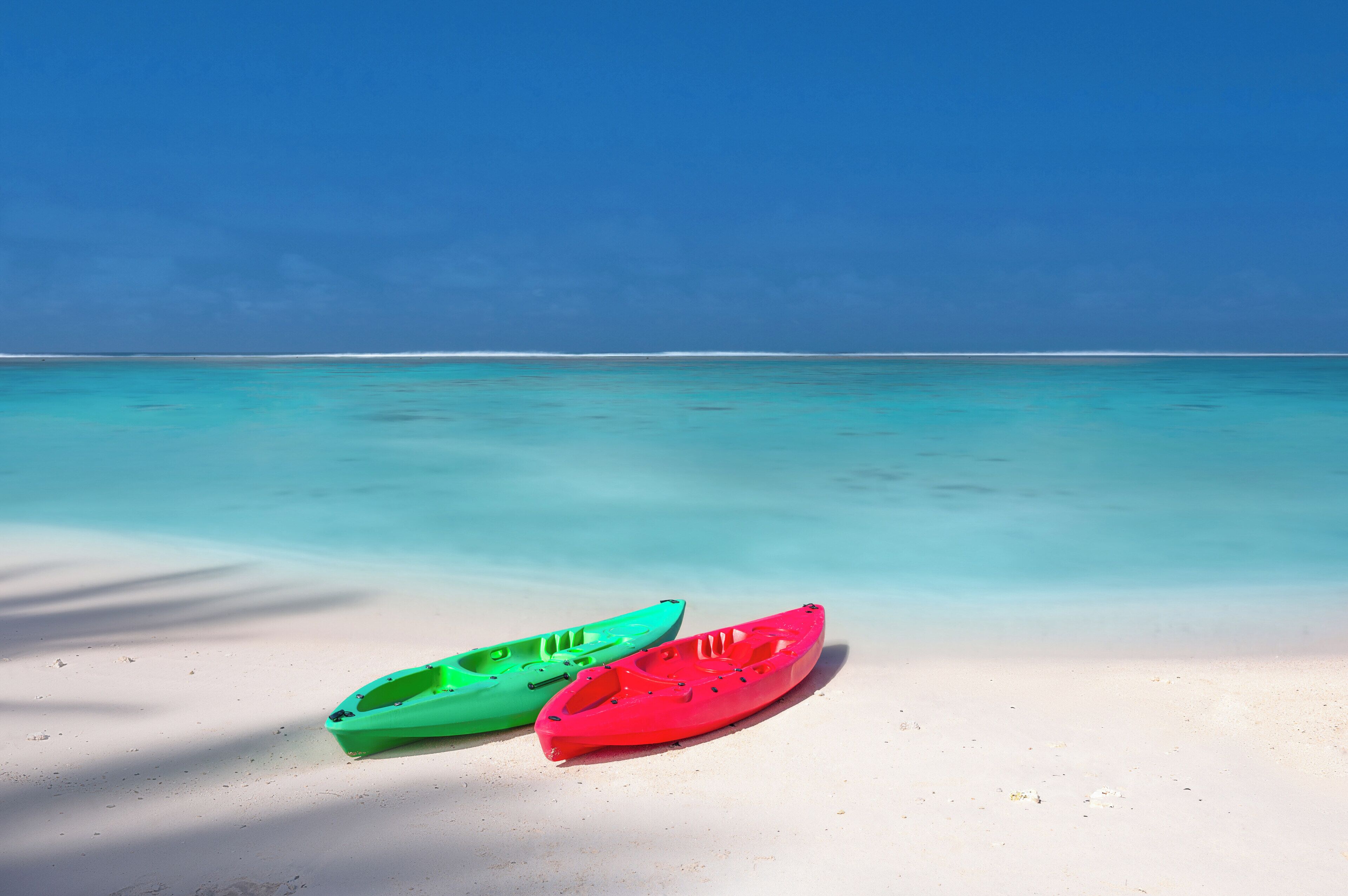 Two kayaks on a sandy beach with clear turquoise water and a blue sky.