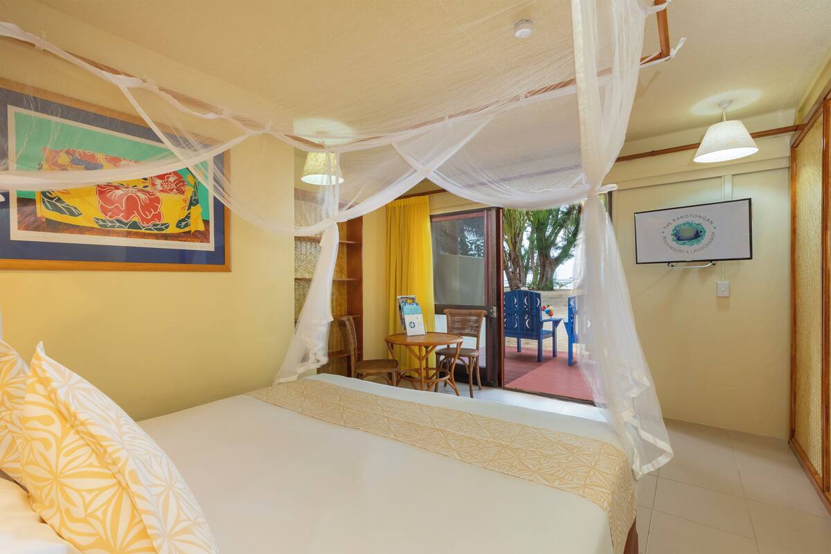 A room with a bed, a desk, and a chair. There is a window and a door leading to an outdoor area.