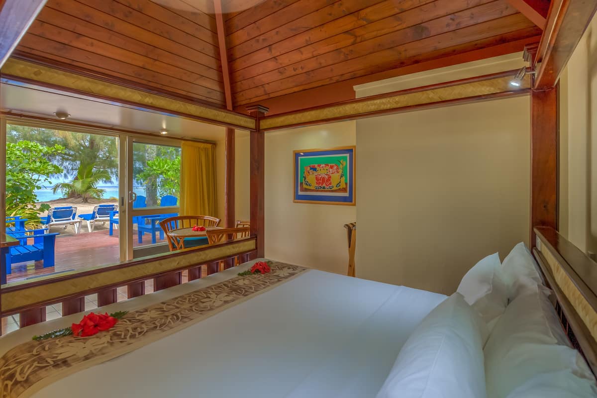 A hotel room with a large bed, wooden ceiling, a view of the outdoor seating area, and a framed picture on the wall.