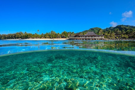 A clear view of a resort with overwater bungalows, a beach, and a mountainous backdrop.