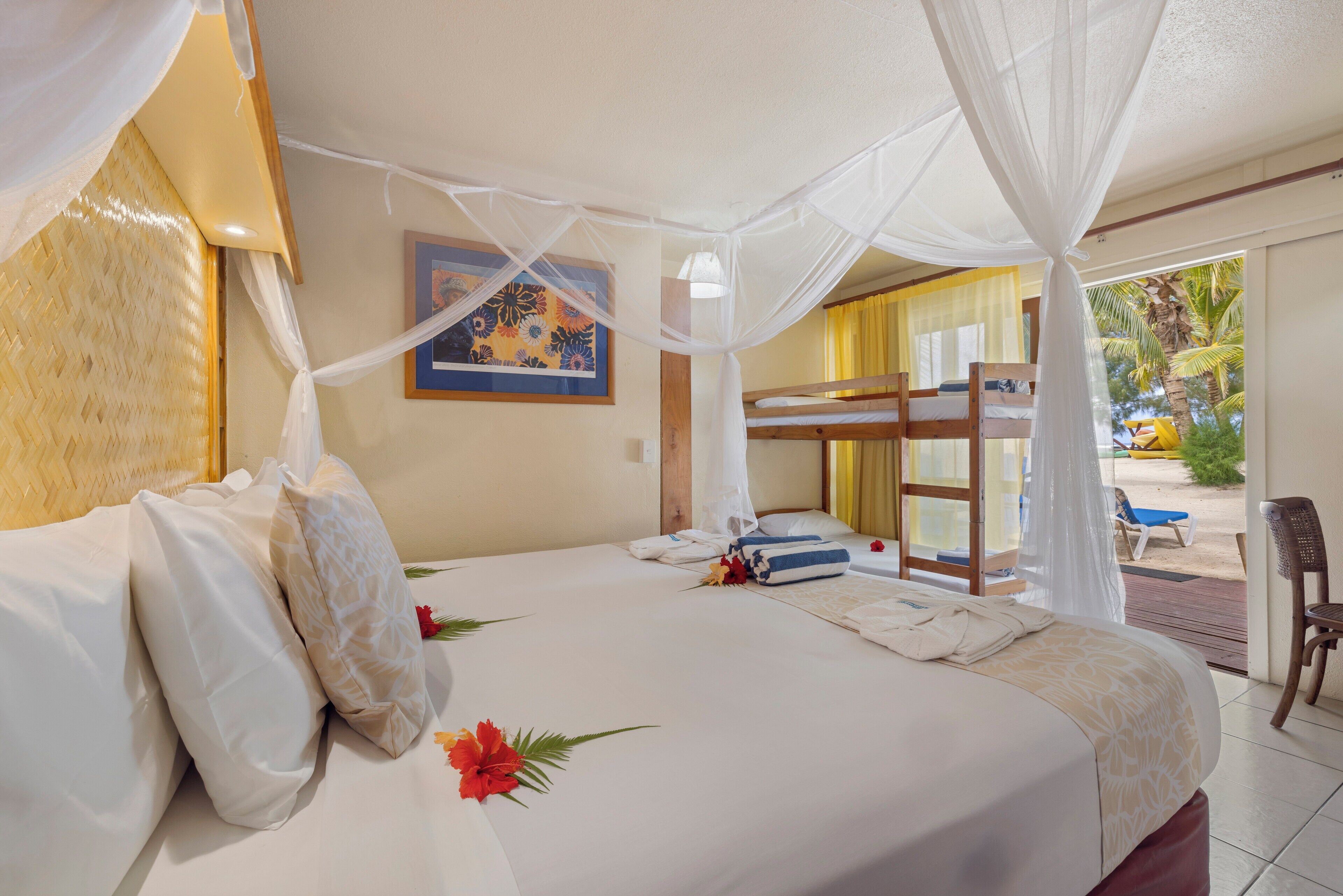 A hotel room with a bed, a bunk bed, a painting on the wall, and a view of the outdoors.