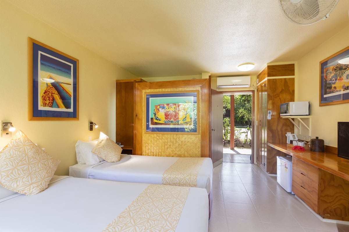 A hotel room with two beds, a kitchenette, and artwork on the walls.