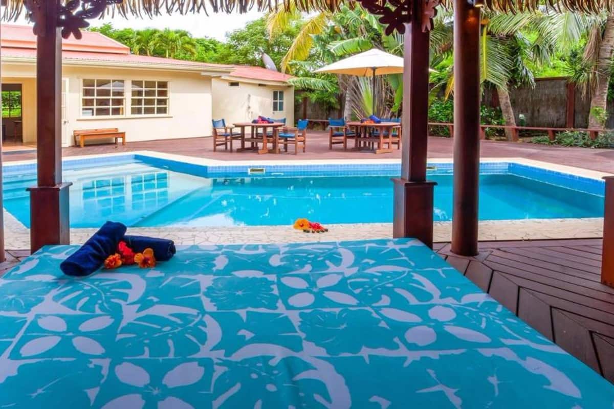 A pool area with a wooden deck, lounge chairs, and a covered seating area with a table.