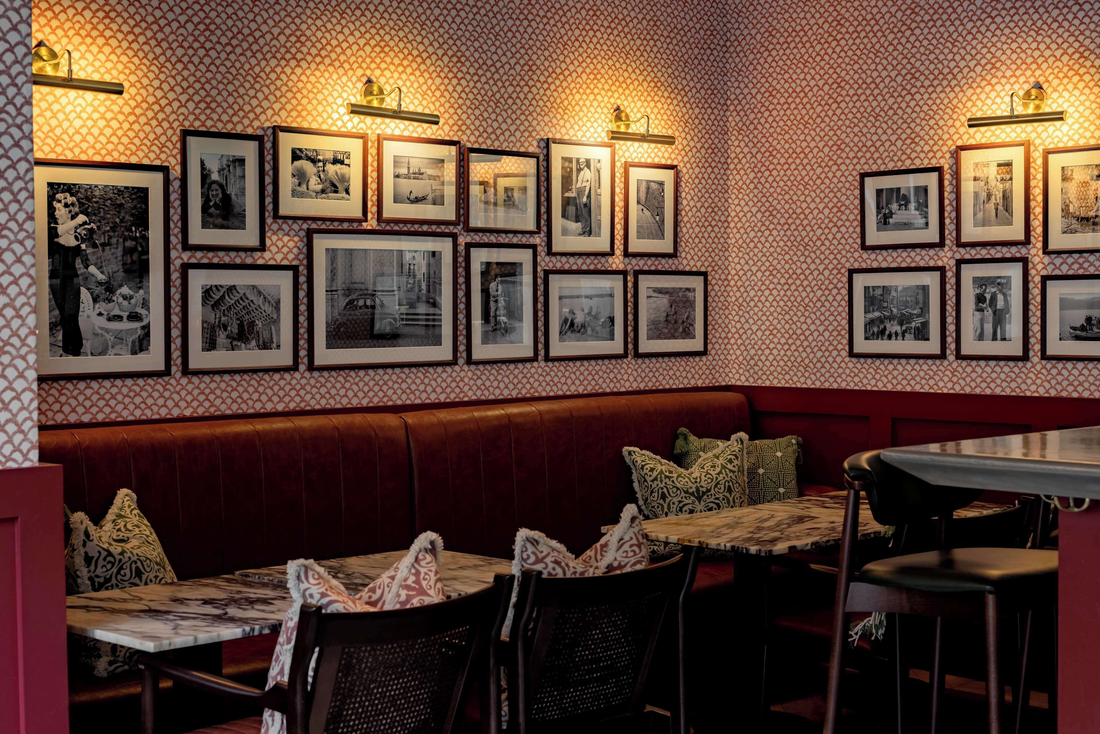 A restaurant with a patterned wall, framed pictures, a red booth, and tables with patterned tablecloths.