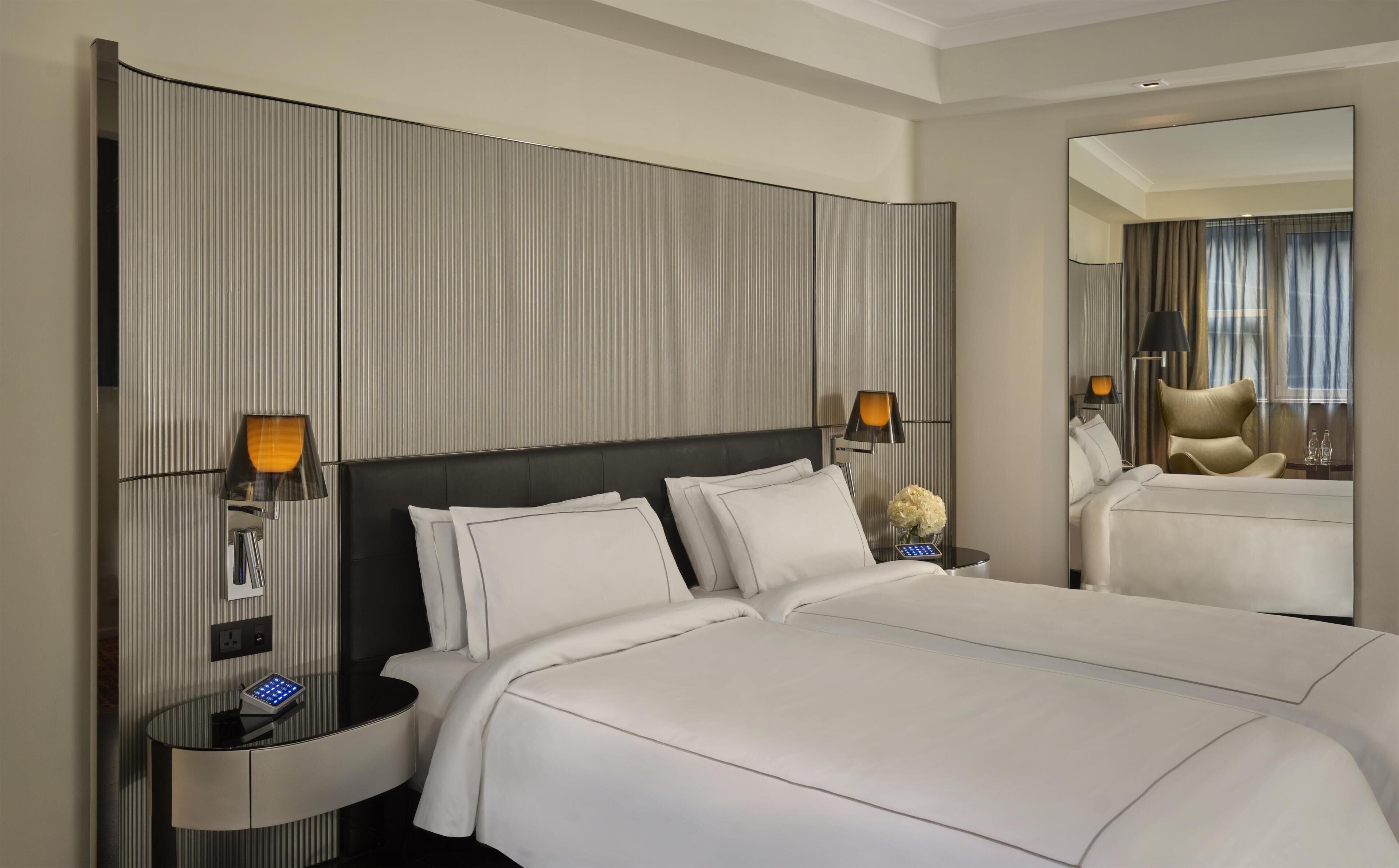 Habitación de hotel con una cama grande, dos mesitas de noche con lámparas, un espejo y vista al interior de la habitación.