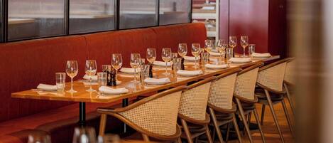 A restaurant with a long wooden table set for a meal, wicker chairs, and a red cushioned bench.