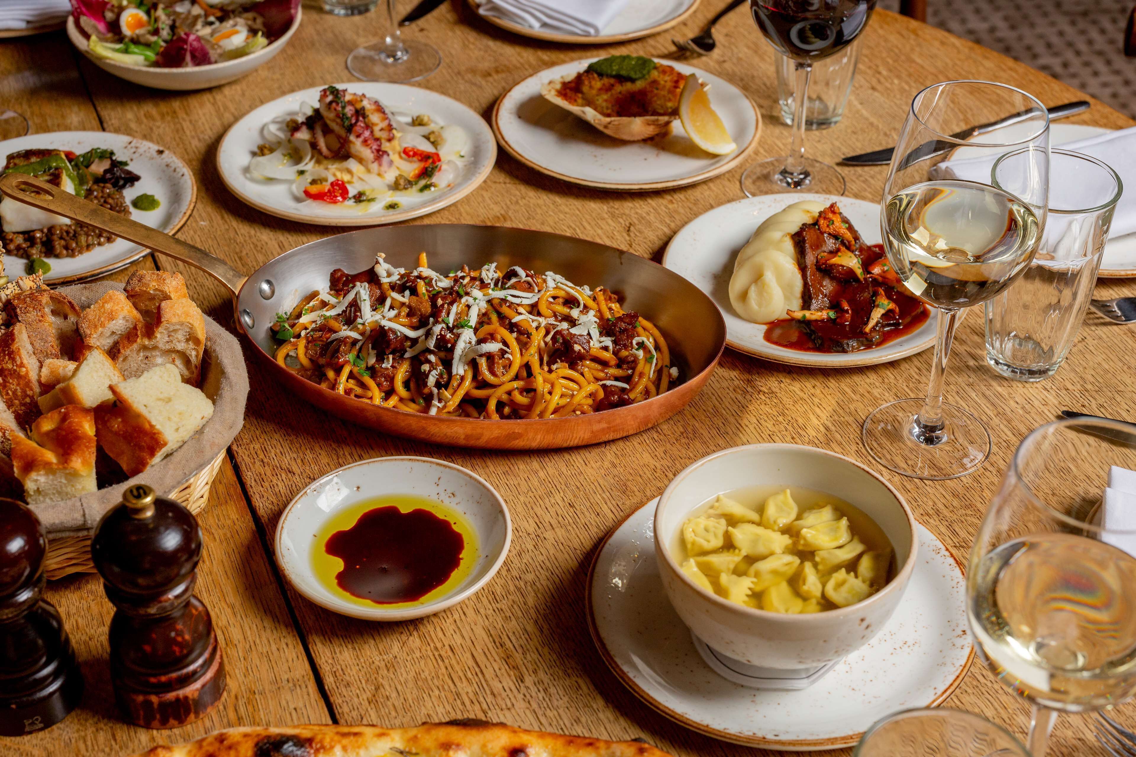 A wooden table with various dishes, including pasta, bread, and a bowl of potatoes.