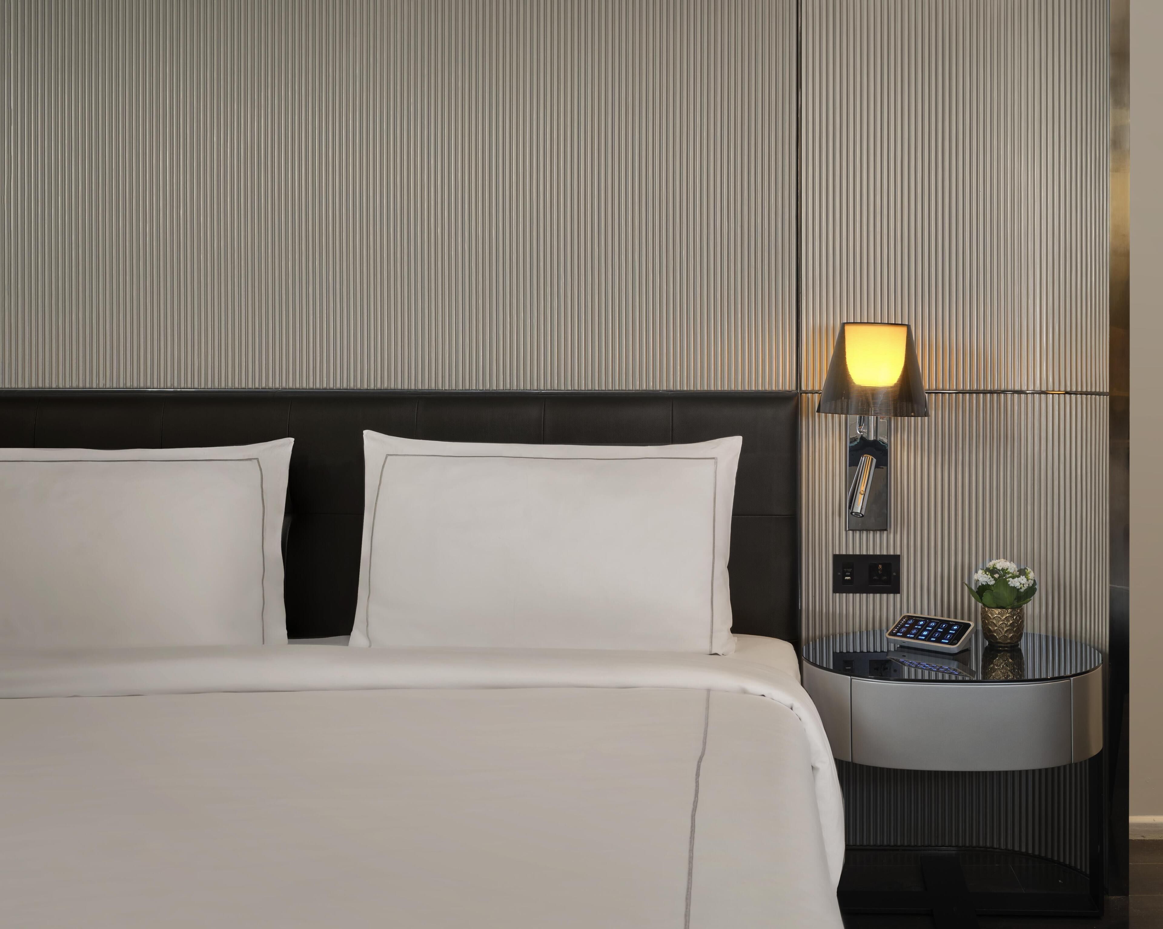 Een moderne hotelkamer met een groot bed, een nachtkastje met een lamp en een klein tafeltje met een vaas.