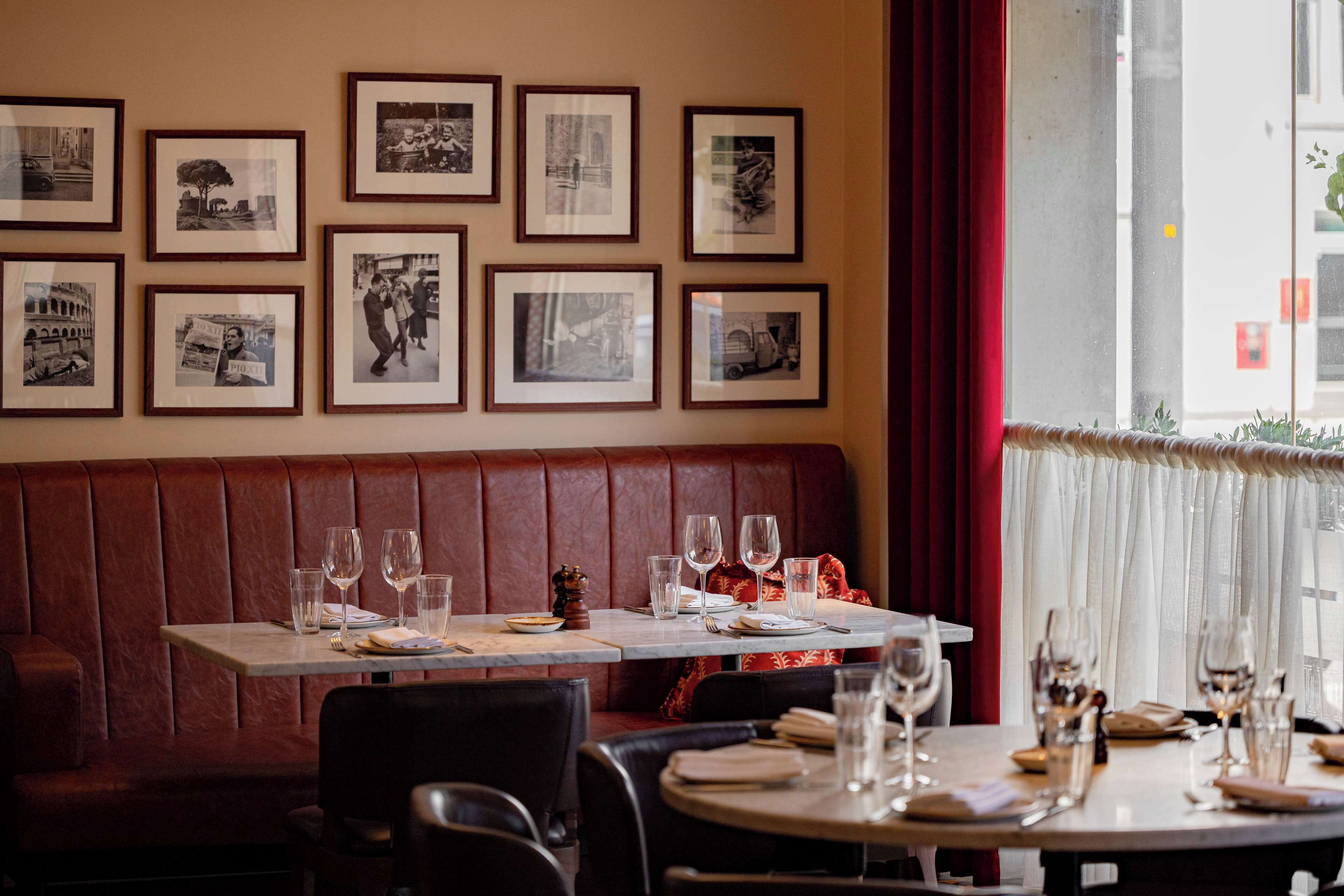 Ein Restaurantinneres mit einer roten Lederausstattung, Esstischen mit leeren Weingläsern und gerahmten Schwarz-Weiß-Fotos an der Wand.