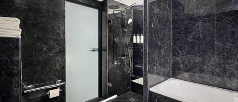 Un baño moderno con ducha envuelta en vidrio, una bañera blanca y pared revestida de mármol.