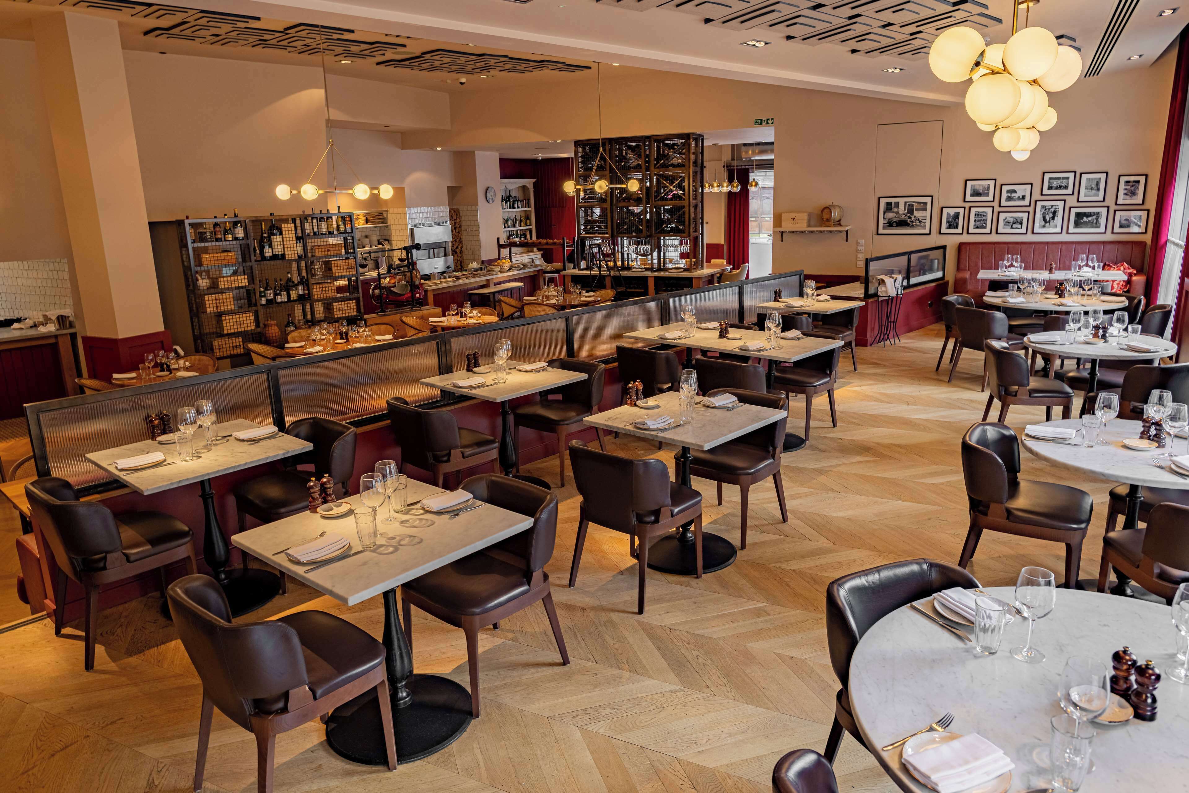Un restaurant doté de plusieurs espaces de restauration, notamment des banquettes et des tables, ainsi qu’un bar avec des étagères remplies de bouteilles.