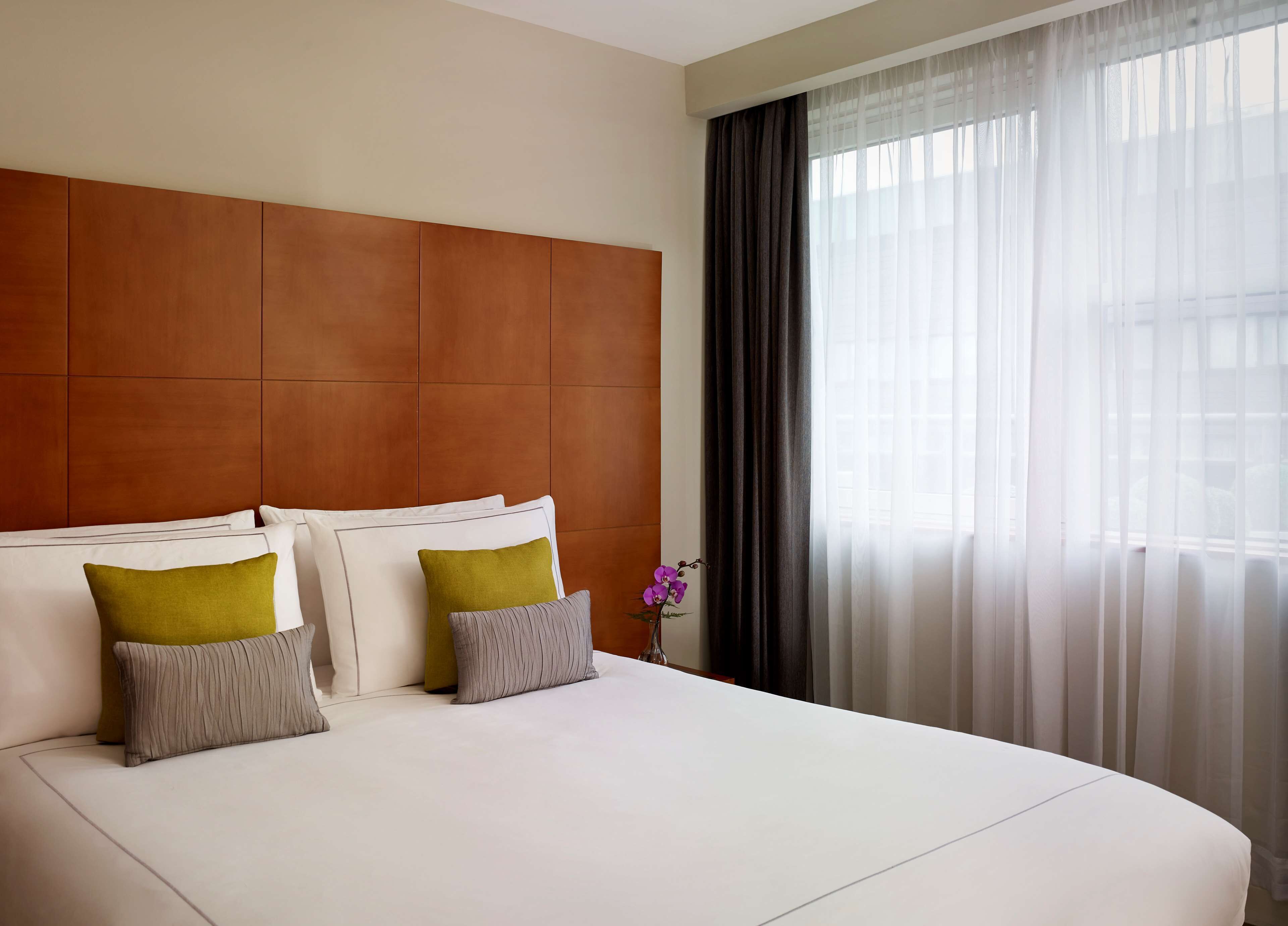 A hotel room with a large bed, a wooden headboard, and sheer curtains.