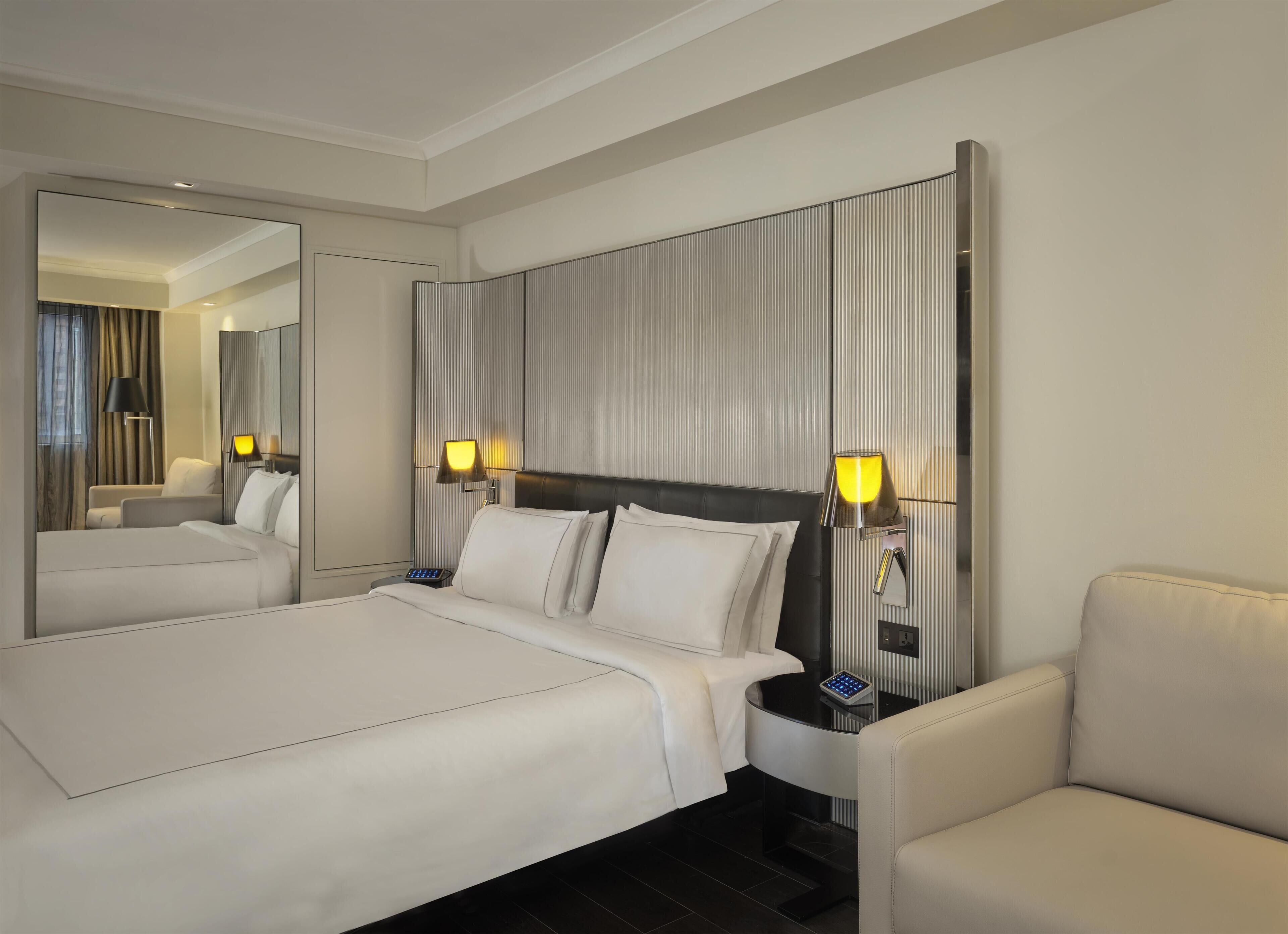 Une chambre d’hôtel avec un grand lit, deux tables de chevet avec des lampes, une chaise et un miroir.