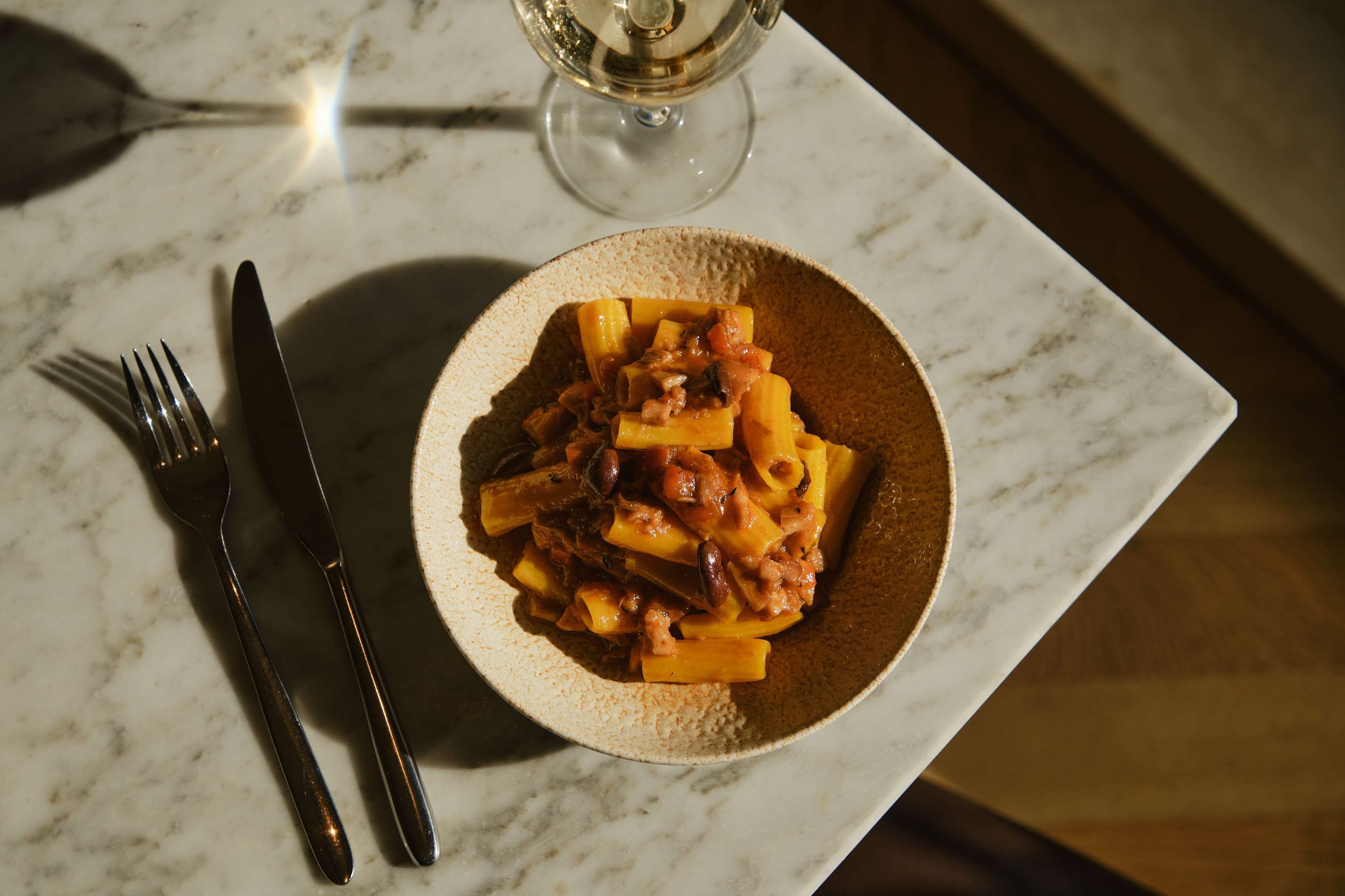 A plate of pasta with a glass of white wine on a marble table.