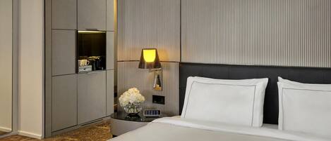 A hotel room with a bed, a nightstand with a lamp, a minibar, and a large wardrobe.