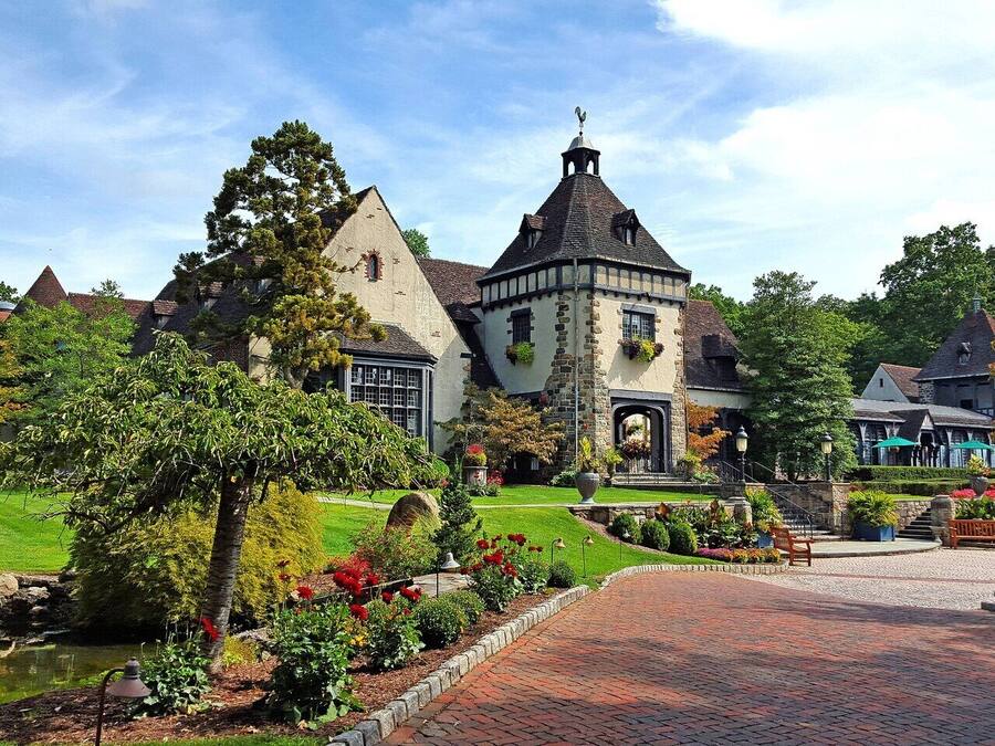 A historic building with a prominent tower, surrounded by well-maintained gardens and a paved walkway.