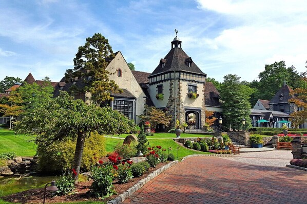 A historic building with a prominent tower, surrounded by well-maintained gardens and a paved walkway.