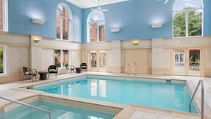 A large indoor swimming pool with clear blue water, surrounded by tiled walls and a high ceiling.