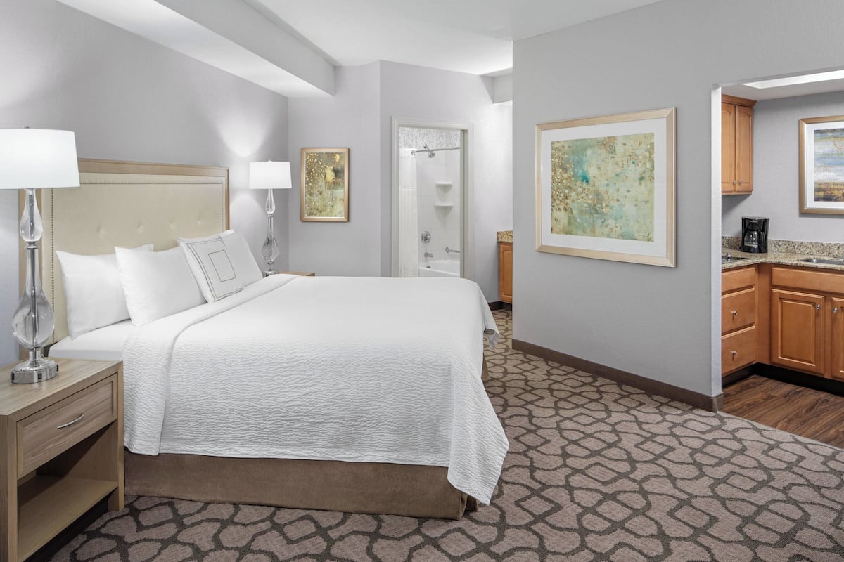 Ein Hotelzimmer mit einem großen Bett, Nachttischlampen, einem Badezimmer mit Dusche und einer Küchenzeile.