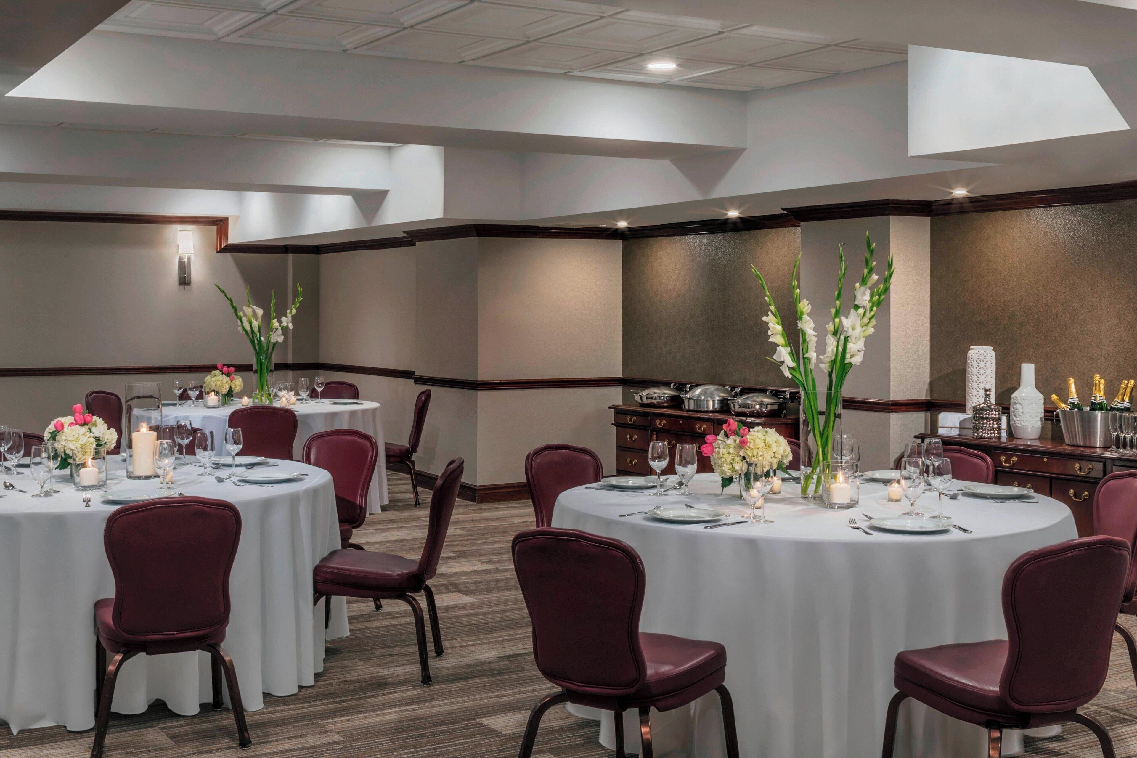 A conference room with round tables, red chairs, and floral centerpieces.