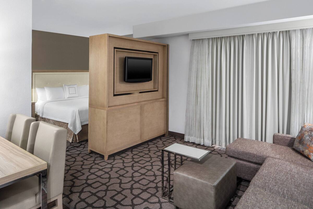 Ein Hotelzimmer mit einem Bett, einem an einer Holzvertäfelung montierten Fernseher, einer Couch, einem kleinen Tisch und einem gemusterten Teppich.
