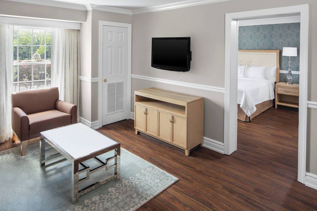 Ein Hotelzimmer mit Bett, Wandfernseher, Holzschrank, Sofa und Tisch.
