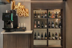 A coffee bar with a coffee machine and a neon sign that reads 'Coffee Bar Open'. There are shelves with various bottles of wine and spirits.