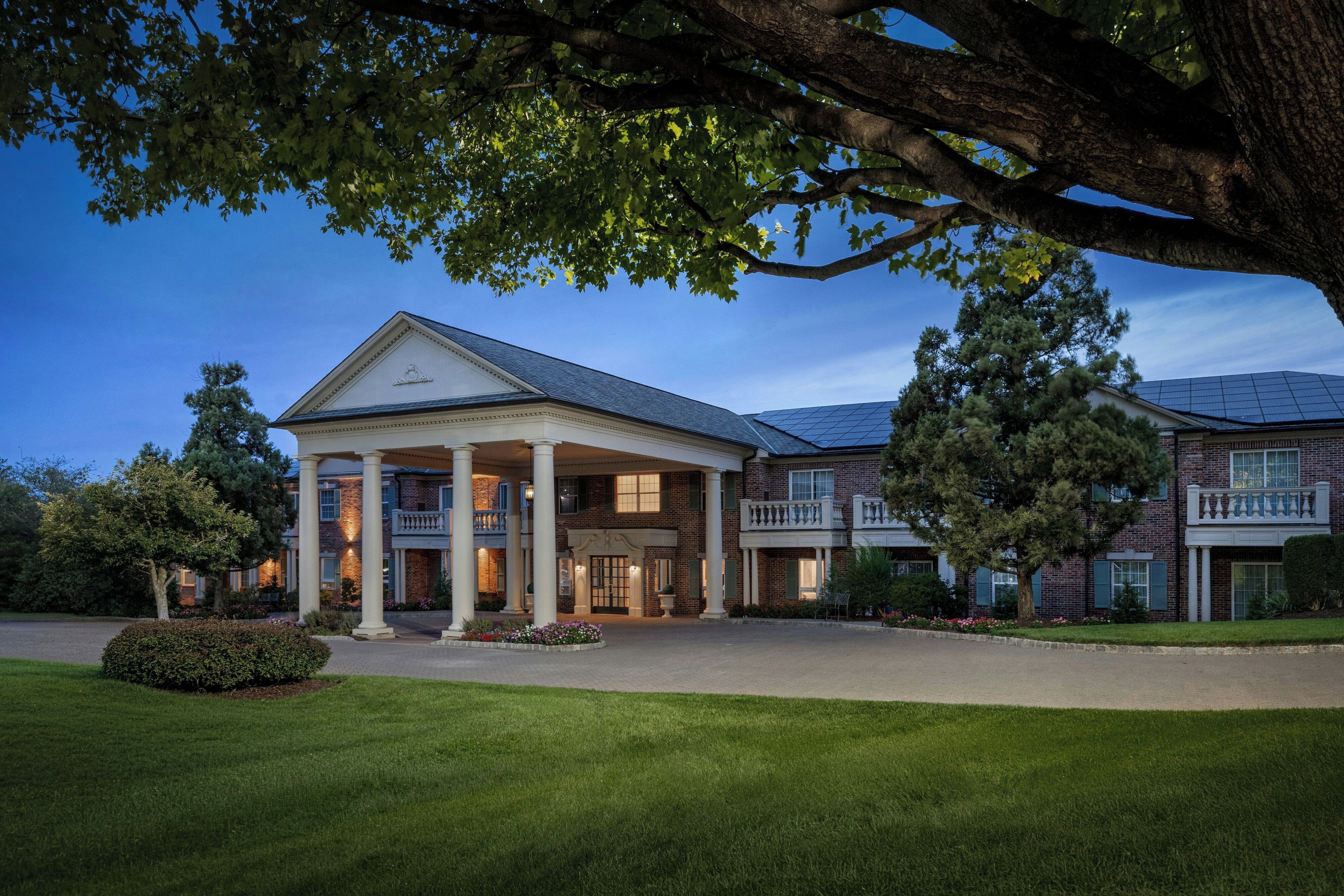 A large, two-story building with a central entrance flanked by columns, surrounded by well-maintained lawns and trees.