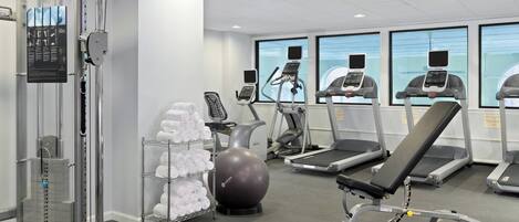 Uma academia com equipamentos de ginástica, um suporte de toalhas na parede e uma grande bola de exercícios.