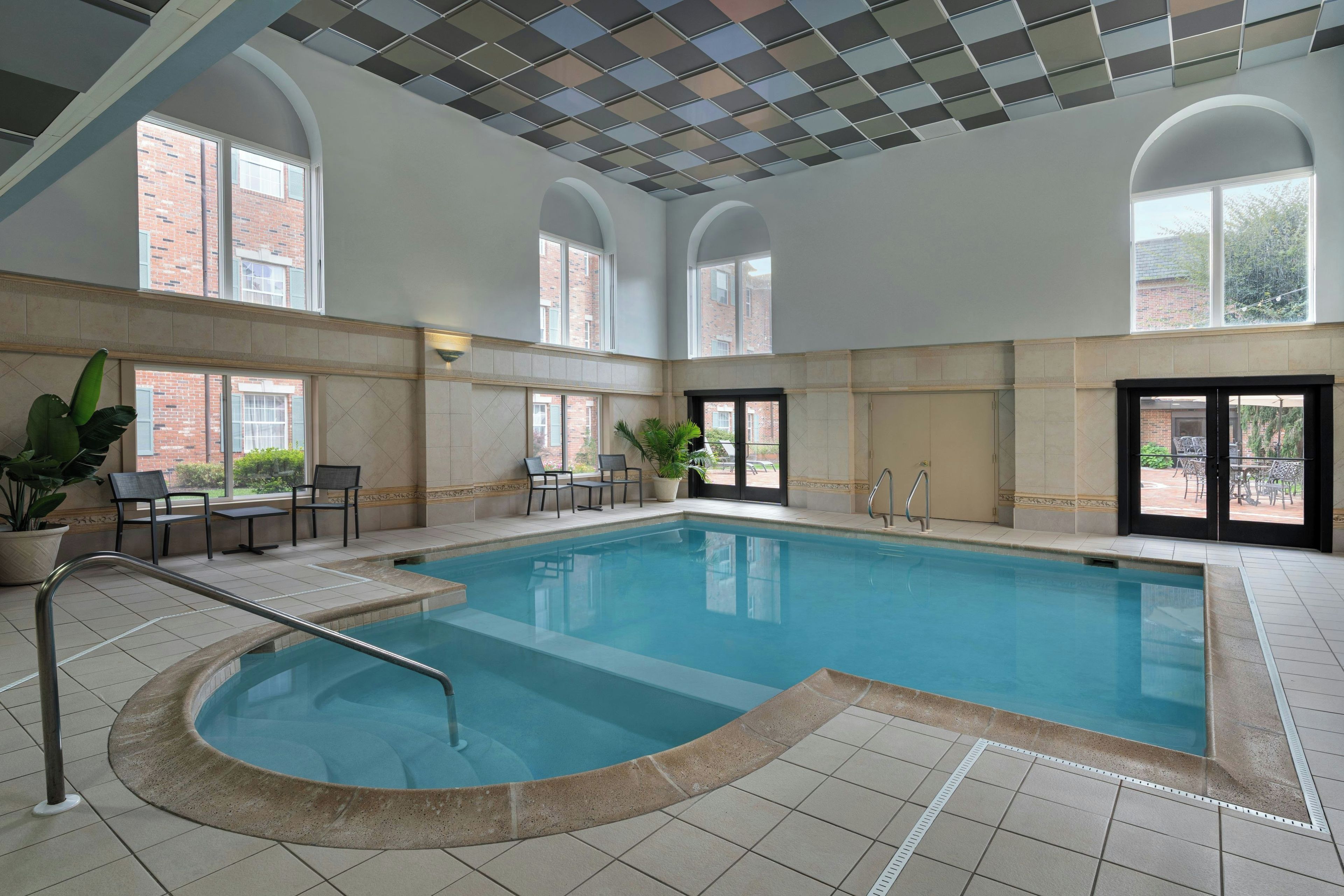 An indoor swimming pool with a tiled floor, a curved edge, and a metal ladder.