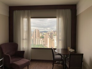 Habitación con vistas a un paisaje urbano, una mesa redonda con sillas y un sillón morado.