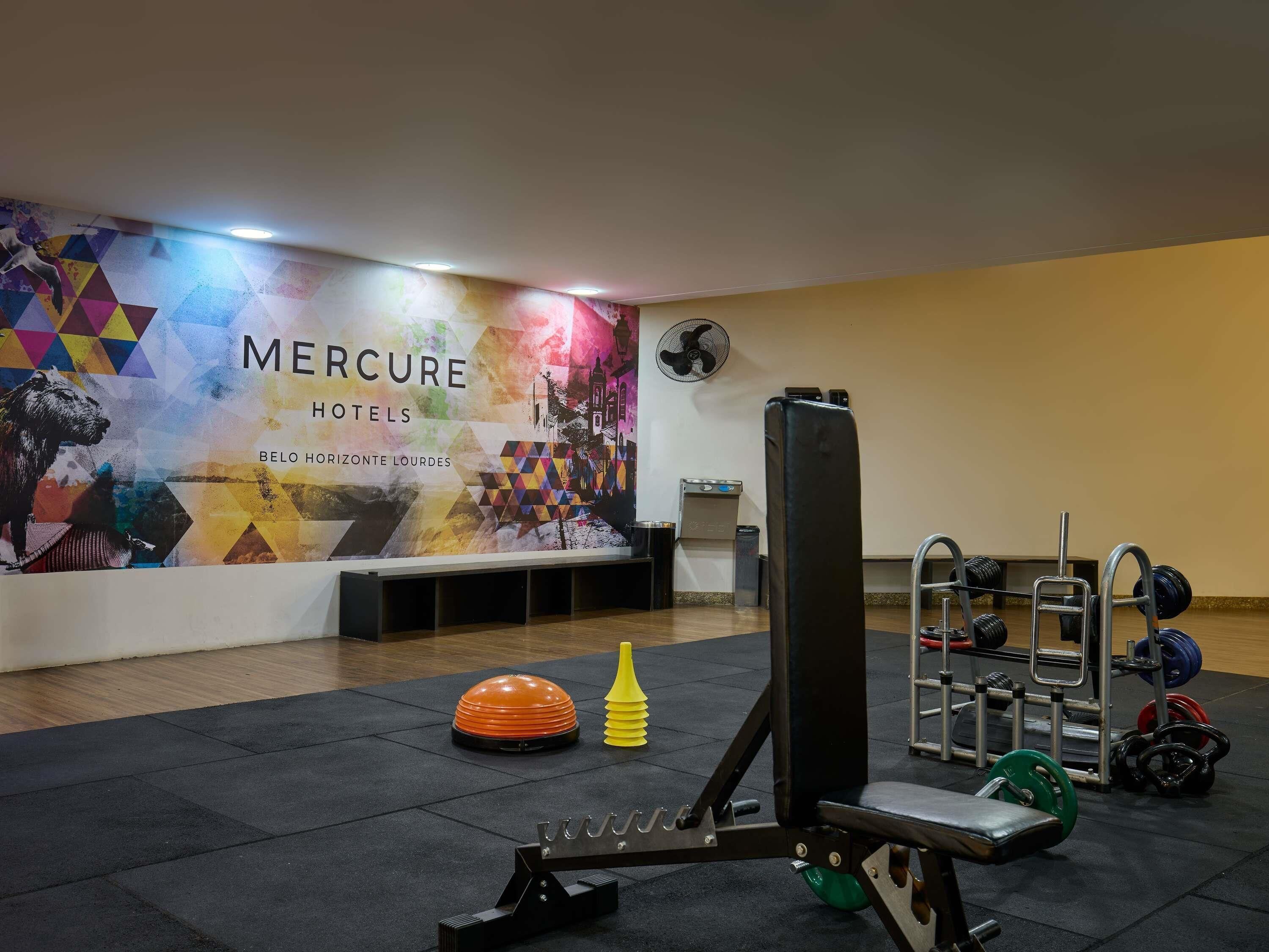 Un gimnasio con equipo de ejercicio, una pared con un mural colorido y un ventilador.