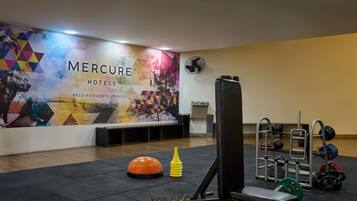 Un gimnasio con equipo de ejercicio, una pared con un mural colorido y un ventilador.