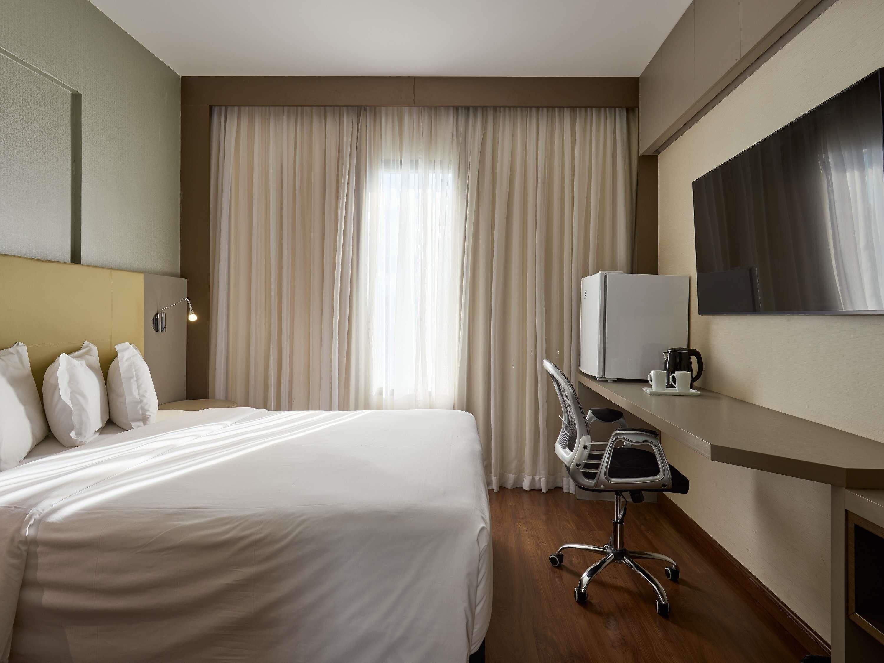 Habitación de hotel con cama, escritorio con computadora, silla y televisor de pantalla plana.