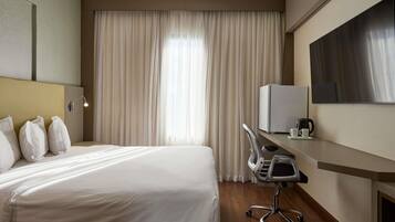 Habitación de hotel con cama, escritorio con computadora, silla y televisor de pantalla plana.