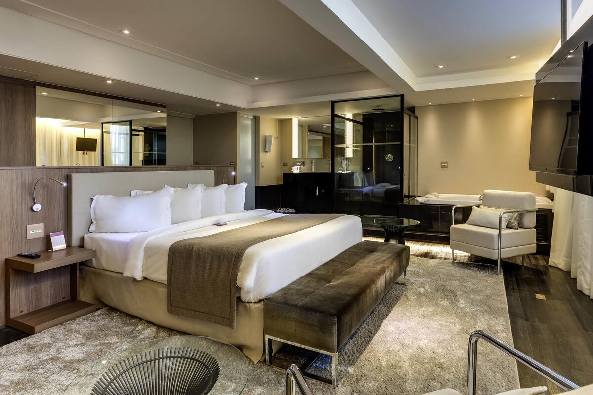 A modern hotel room with a large bed, a desk, a chair, a TV, and a mirror.