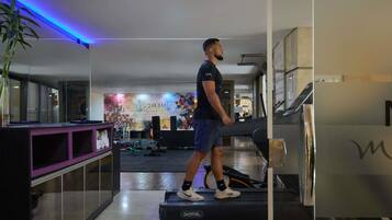 A man walking on a treadmill in a gym with mirrored walls, exercise equipment, and a colorful wall mural.