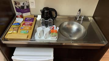 Uma cozinha compacta com pia de aço inoxidável, cafeteira e diversos alimentos.