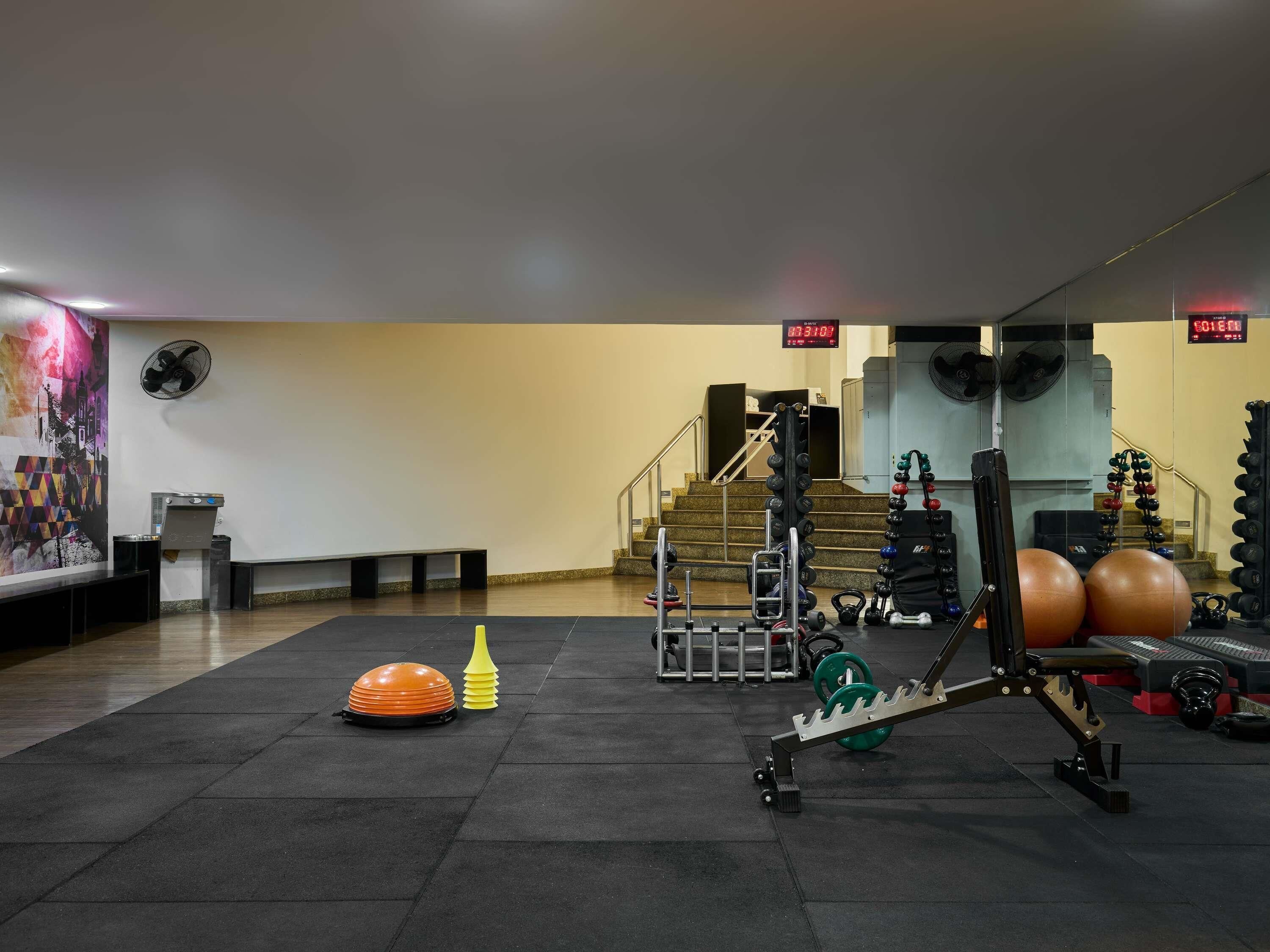 Un gimnasio con equipamiento de levantamiento de pesas, un reloj y una escalera.