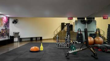 Un gimnasio con equipamiento de levantamiento de pesas, un reloj y una escalera.
