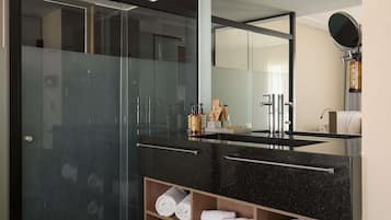 Un baño moderno con cabina de ducha de vidrio, lavamanos de mármol negro y estante de madera con toallas.