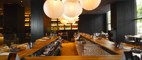 A bar area with wooden flooring, multiple hanging paper lanterns, and a long counter with bar stools.