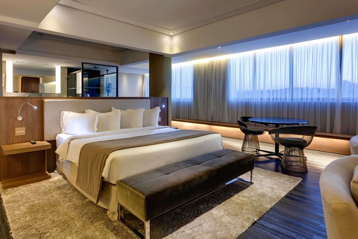 A modern hotel room with a large bed, bedside tables, a desk, and a chair.